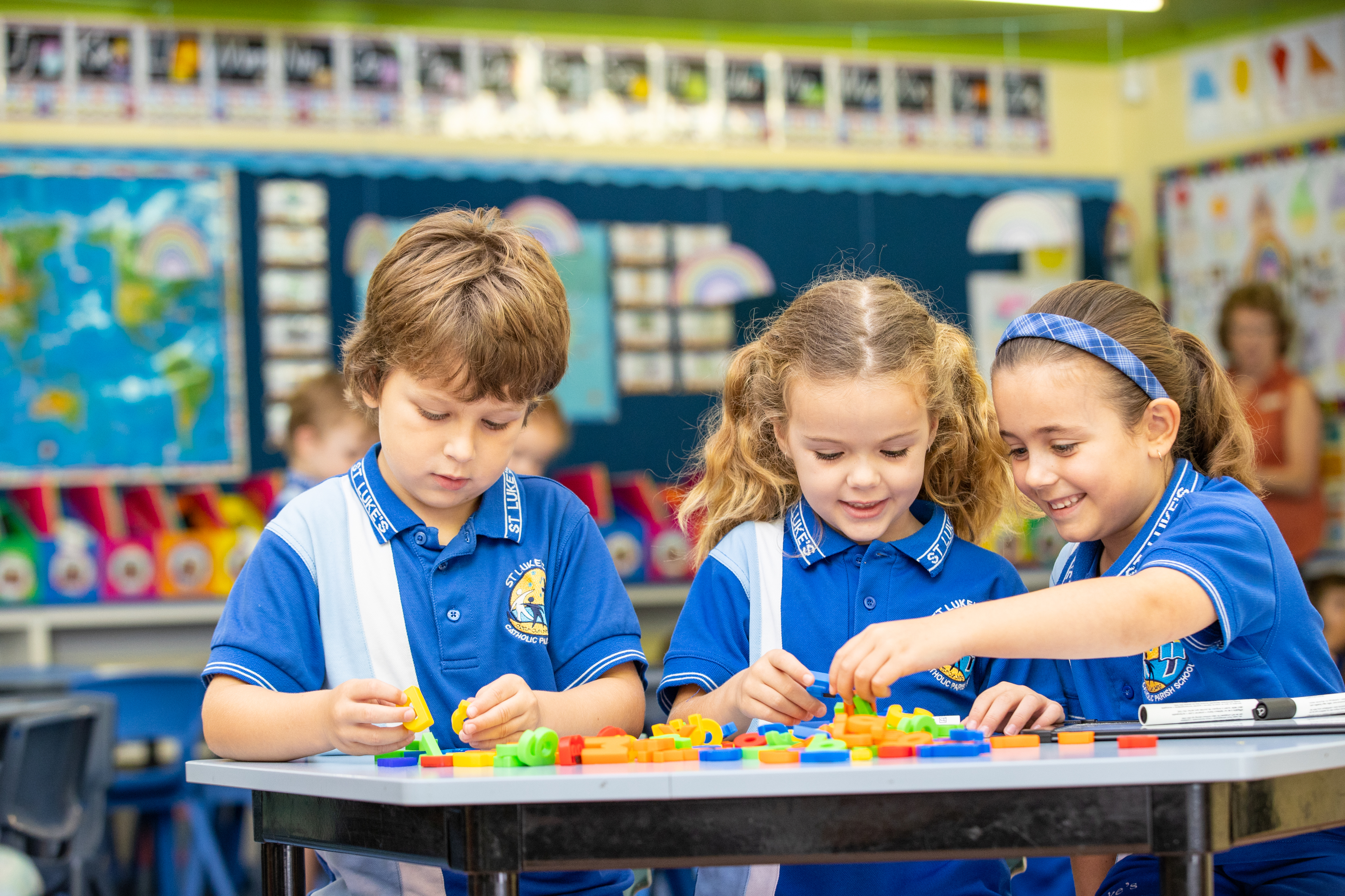 Three students in school uniform working together at a table using colourful letter tiles during a classroom activity.