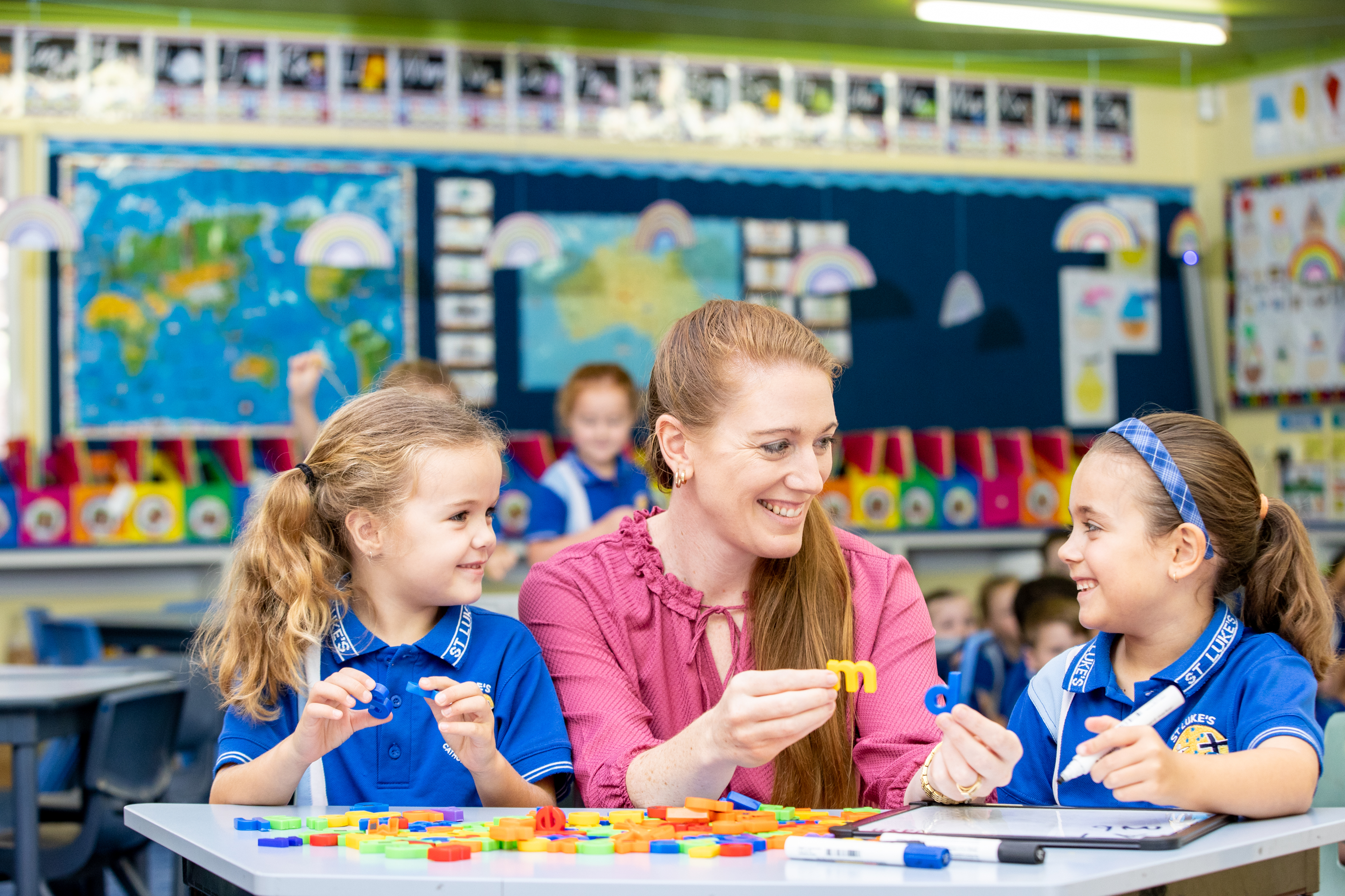 Adult working with two students at a classroom table using colourful letter pieces during a literacy activity.